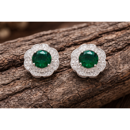 Silver floral halo stud earrings with emerald green centre stones photographed on textured wood