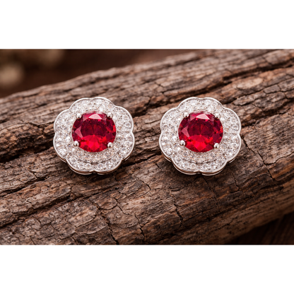 Silver floral halo stud earrings with pinkish red centre stones displayed on rustic wooden surface
