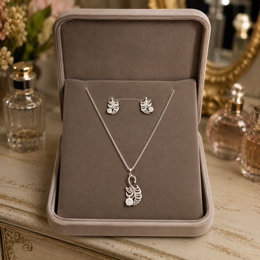 Silver leaf crystal pendant and matching stud earrings displayed inside a premium taupe velvet jewelry box on a vintage chalk-finish dressing table with softly blurred luxury perfume bottles.