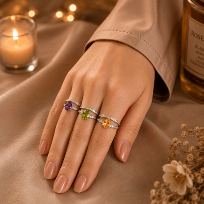 Model wearing three silver split-band rings with purple, green, and peach pear-cut crystal stones in a luxury lifestyle setting by TIAS Collection