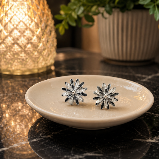 Silver and black rotating floral spinner stud earrings displayed on an ivory ceramic saucer on black marble.