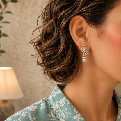 Woman wearing pearl drop earrings with a crystal swirl and floral design, styled with a sea green printed linen shirt.