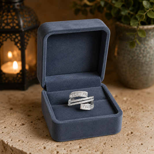 Luxury silver sculpted multi-band statement ring with baguette and pavé crystals displayed in a smoky blue premium jewellery box on travertine stone