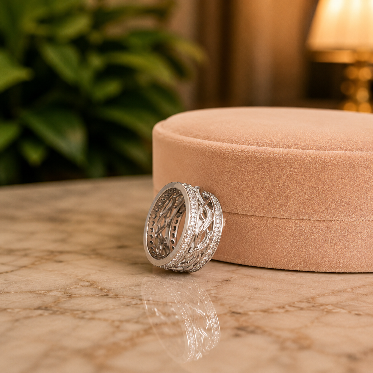 Silver infinity statement ring shown from the side, revealing its intricate openwork band and double zircon borders beside a peachy-cream jewellery box on reflected marble.