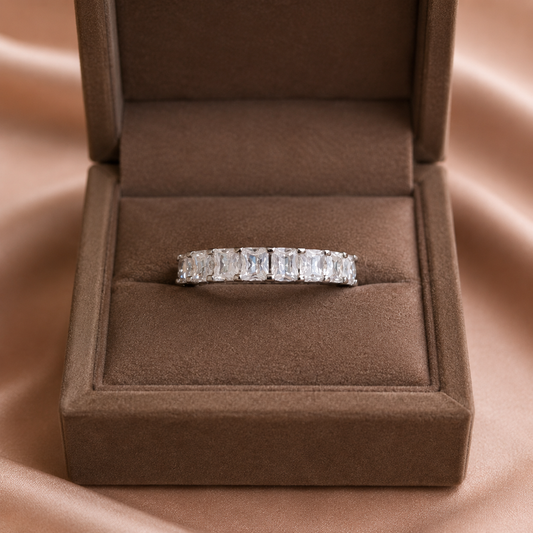 Silver eternity band with emerald-cut clear stones displayed in a premium mocha brown velvet jewelry box on a soft satin backdrop