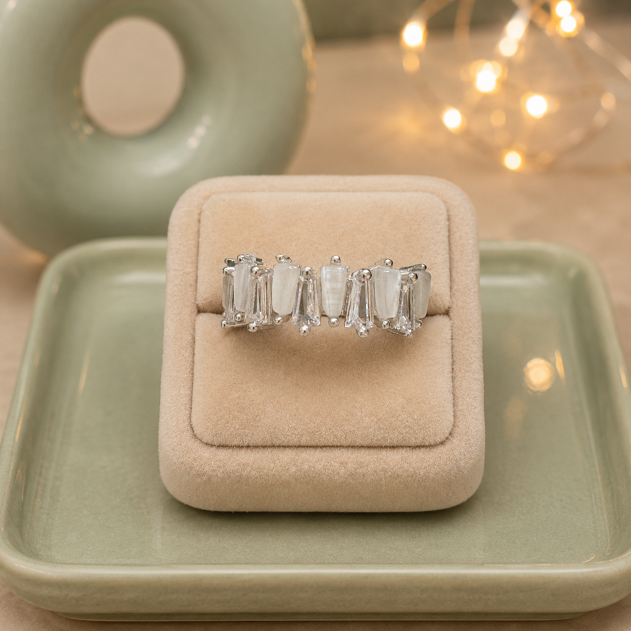 Silver statement ring with natural mother-of-pearl baguette stones displayed on a premium beige velvet ring stand with a sage green ceramic tray.