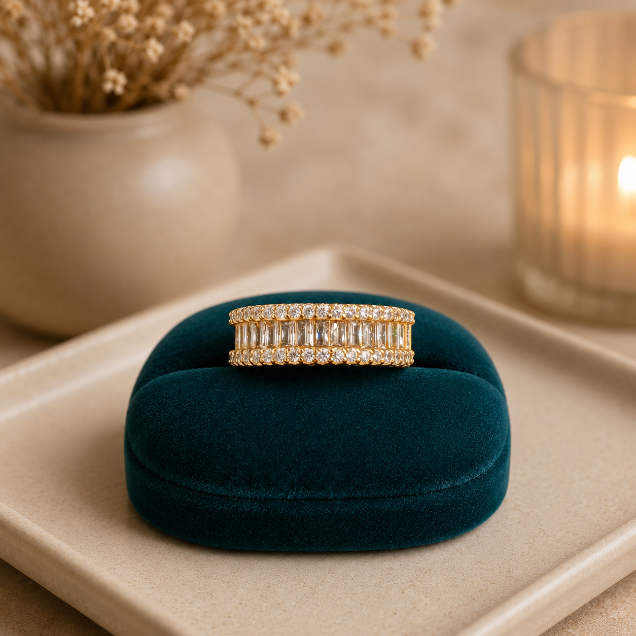Gold baguette crystal statement band displayed on a premium teal velvet stand on a neutral ceramic tray with candle and dried flowers.