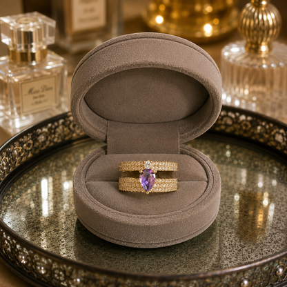 Light gold open-back double-band ring featuring a pear-cut purple centre stone with sparkling zircon detailing displayed in a luxury taupe velvet jewellery box.