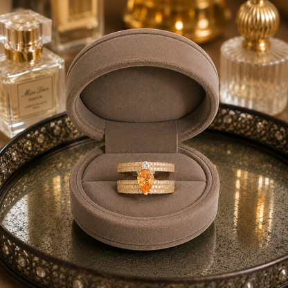 Light gold open-back double-band ring featuring a pear-cut champagne centre stone with sparkling zircon detailing displayed in a luxury taupe velvet jewellery box.