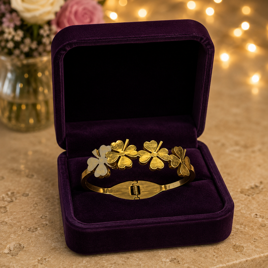 Gold four-leaf clover magnetic cuff bracelet displayed inside a premium royal plum velvet jewellery case on a travertine surface.