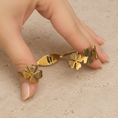 Close-up of a gold four-leaf clover bracelet with an easy front magnetic clasp shown open on a luxury travertine surface.