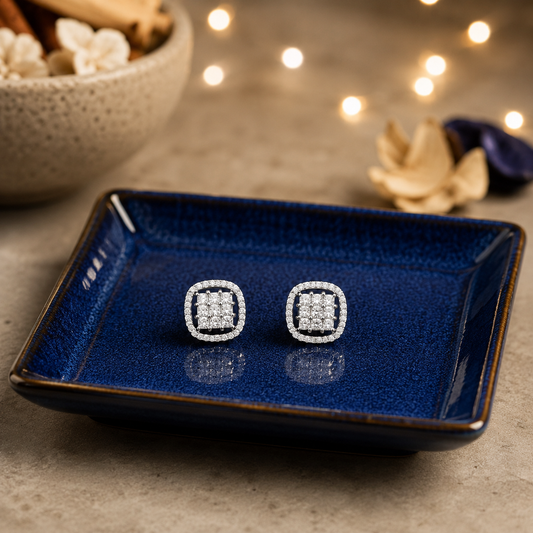 Square halo crystal stud earrings displayed on a royal blue ceramic plate with a luxury concrete background and softly blurred fairy lights