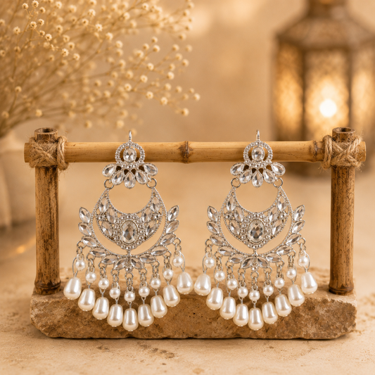 Silver ethnic chandelier earrings with pearl drops hanging on a rustic bamboo display with warm décor background.