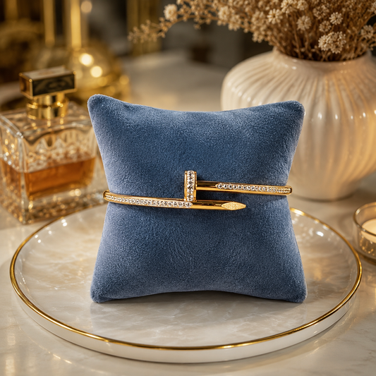 Premium gold nail lock crystal cuff bracelet displayed on a luxury smoky blue velvet cushion in a boutique-style jewelry presentation