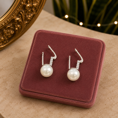 Silver crystal and pearl leverback earrings displayed open on a premium dusty rose velvet jewelry stand with a luxury marble background.