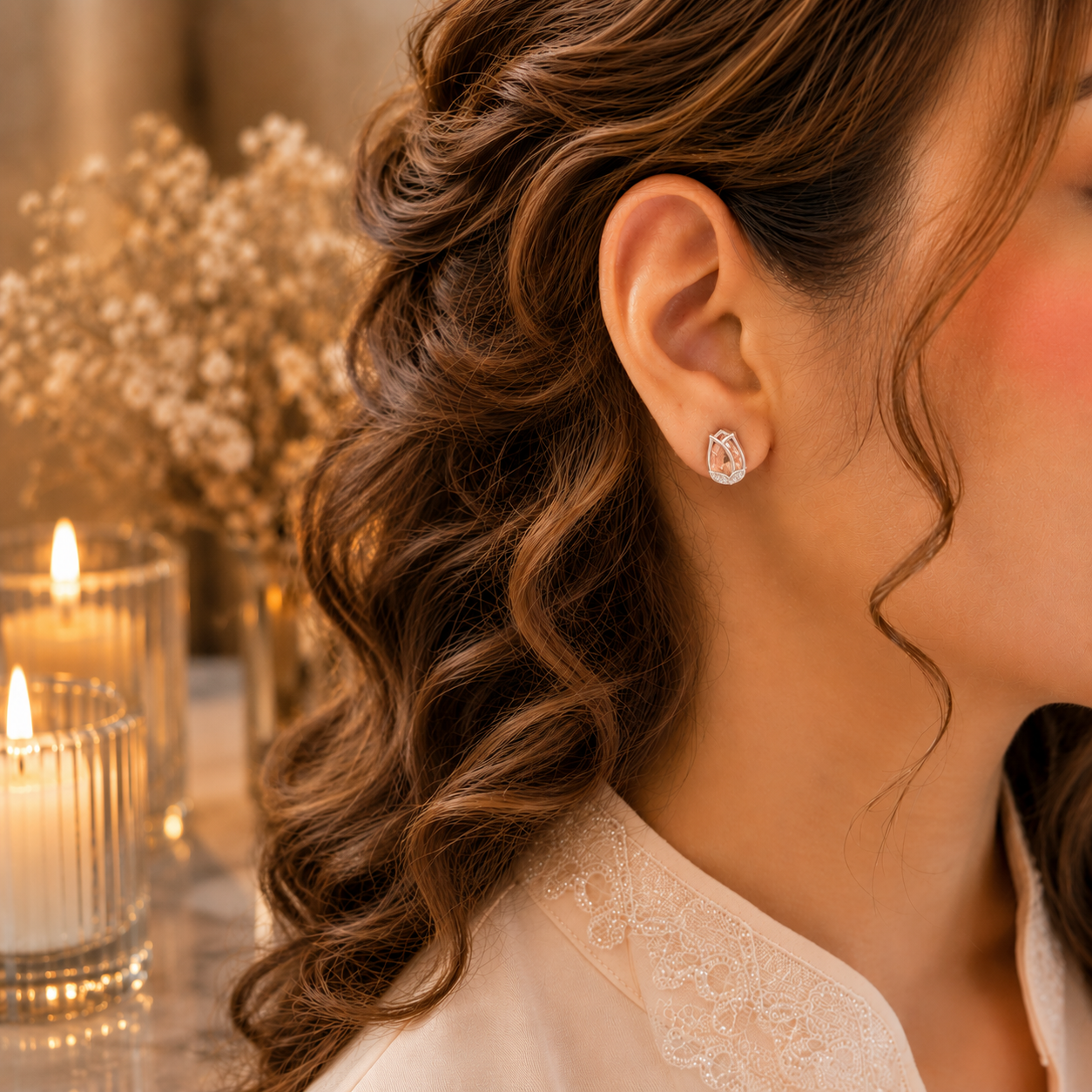 Woman wearing tulip crystal stud earrings in a luxury close-up portrait with soft curls, ivory-peach outfit, warm candlelight and dried floral background