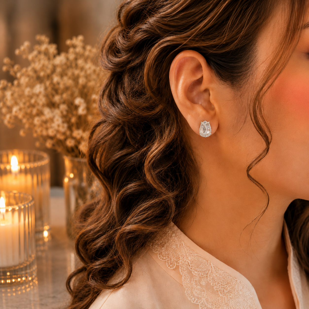 Woman wearing tulip crystal stud earrings in a luxury close-up portrait with soft curls, ivory-peach outfit, warm candlelight and dried floral background
