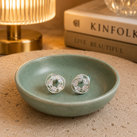 Silver interlocking circle zircon stud earrings displayed in a premium sea green ceramic bowl on textured limestone with soft studio lighting and luxury décor background.