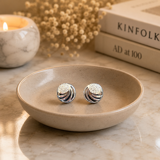 Silver swirl crystal stud earrings displayed on a premium greige jewellery stand, featuring polished silver metal with shimmering zircon crystals for luxury jewellery photography.