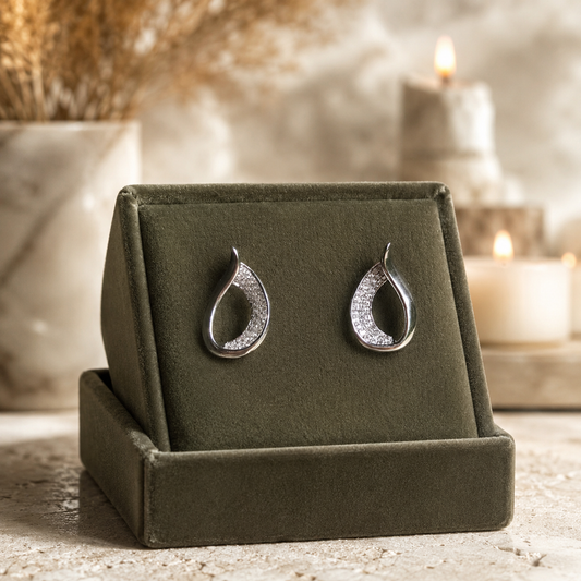 Silver teardrop crystal earrings on an olive green velvet jewellery stand with a softly blurred luxury background.
