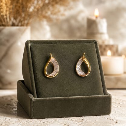 Gold teardrop crystal earrings on an olive green velvet jewellery stand with a softly blurred luxury background.
