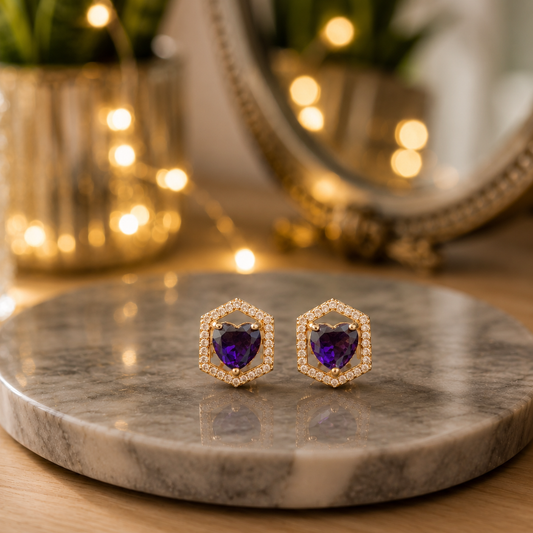Royal purple heart crystal hexagon stud earrings displayed on a polished grey marble slab with a softly blurred luxury background.