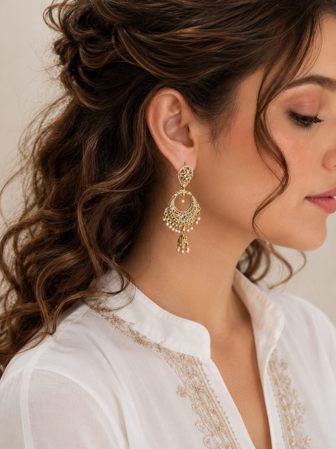 Woman wearing antique gold Chandbali earrings with ivory pearl tassels, traditional statement jewelry with intricate filigree detailing.