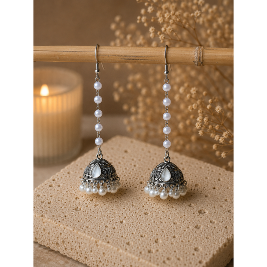 Pair of silver and pearl earrings on a wooden surface with a candle in the background