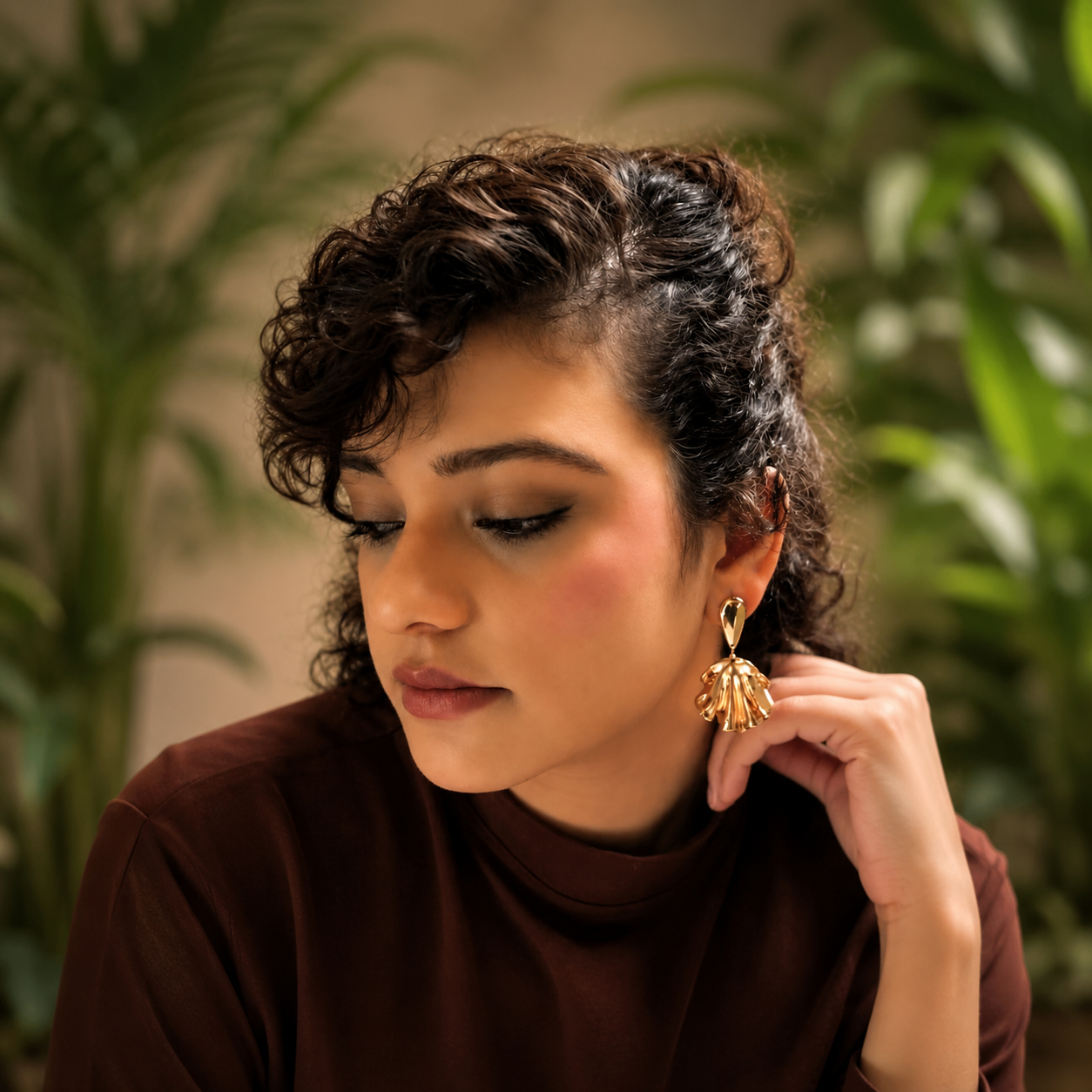 Woman wearing a gold earring with a blurred green plant background
