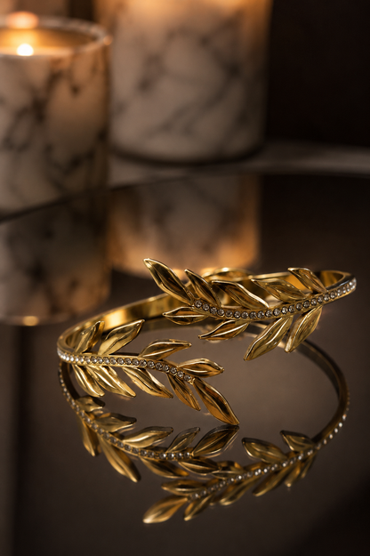 Gold leaf bracelet on a reflective surface with blurred candles in the background