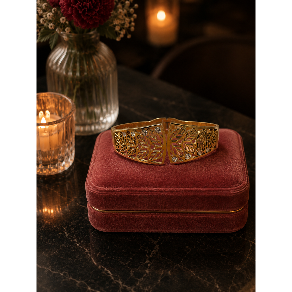Gold-tone botanical magnetic cuff bracelet with crystal accents displayed on a pink velvet bracelet stand on a black marble restaurant table with candlelight and floral décor.