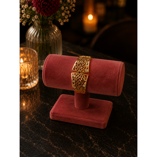 Gold-tone botanical magnetic cuff bracelet with crystal accents displayed on a pink velvet bracelet stand on a black marble restaurant table with candlelight and floral décor.