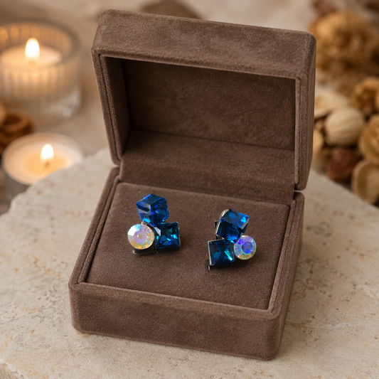 Blue crystal earrings in a brown velvet box with candles and dried flowers in the background