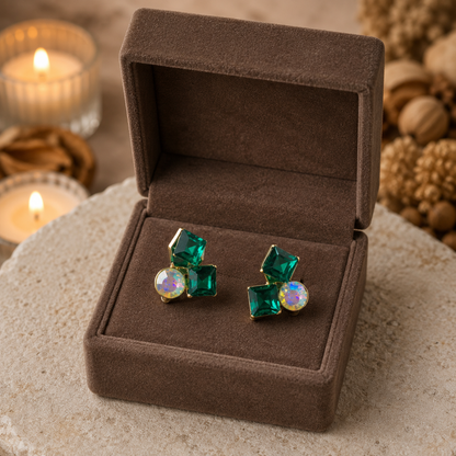 Green gemstone earrings in a brown jewelry box with candles and decorative elements in the background