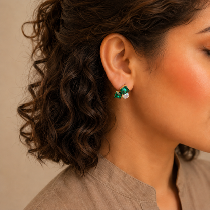 Model wearing emerald green geometric crystal stud earrings with gold-tone finish in a side-profile portrait.