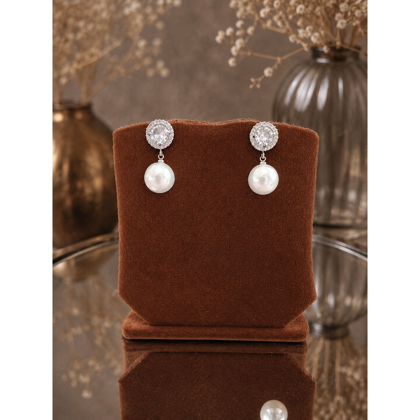 Pearl drop earrings with crystal halo studs displayed on a premium copper-brown velvet jewelry stand against a softly blurred luxury background