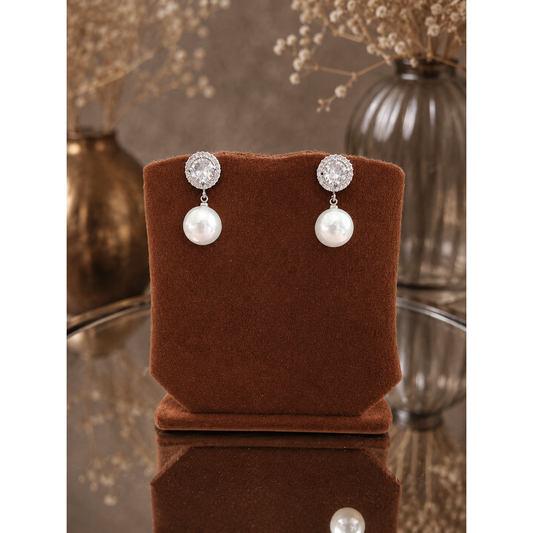 Pearl drop earrings with crystal halo studs displayed on a premium copper-brown velvet jewelry stand against a softly blurred luxury background