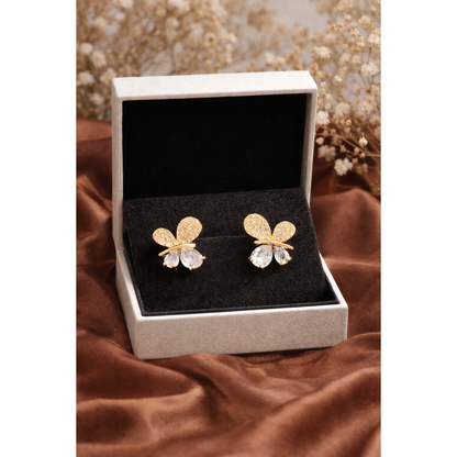 Butterfly stud earrings displayed in jewelry box on brown silk cloth with blurred dry flowers background in gold and silver stone variant