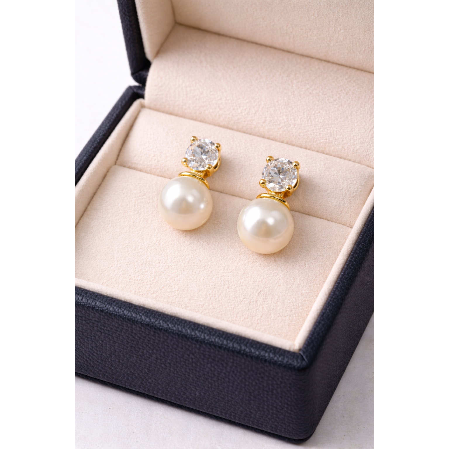 Gold pearl and zircon drop earrings displayed in cream velvet jewelry box with warm reflective shine