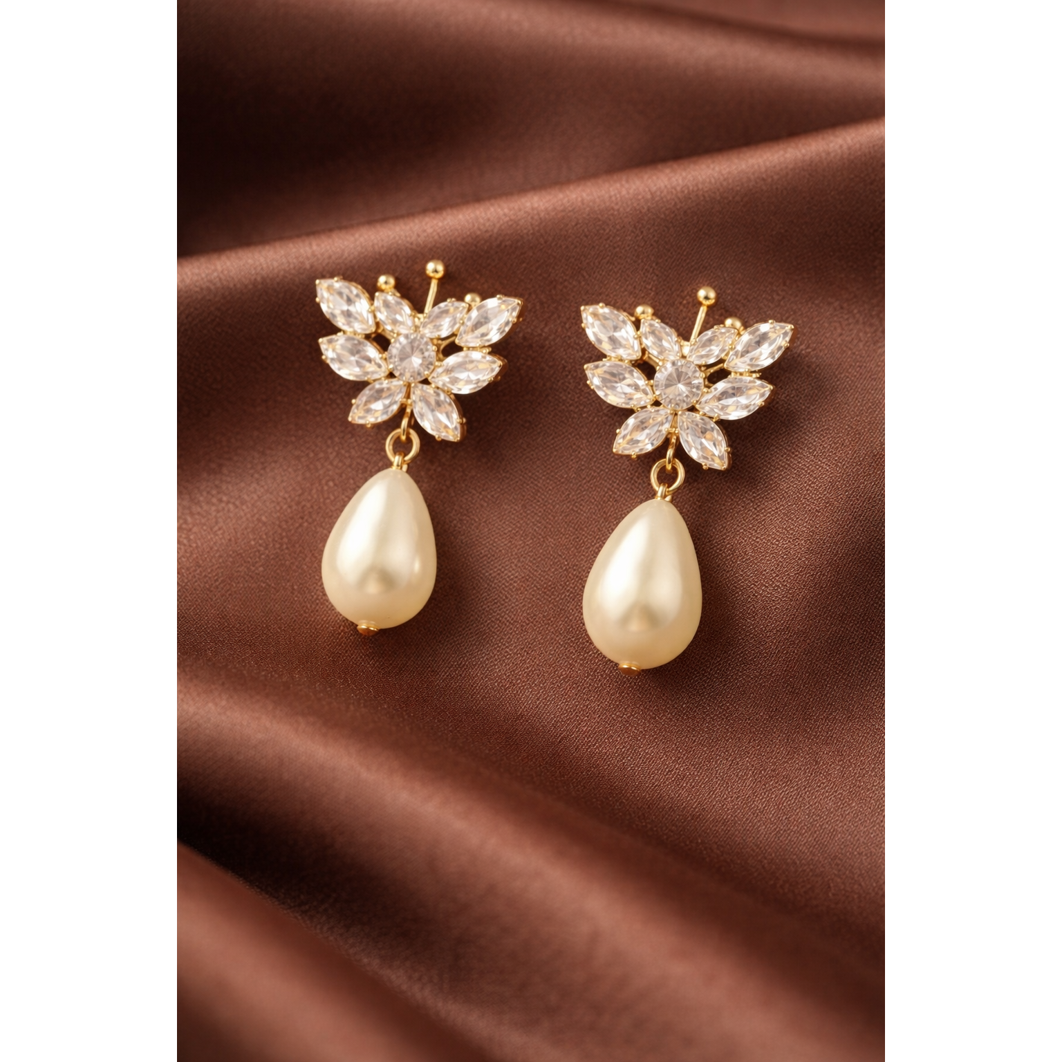 Gold butterfly crystal pearl drop earrings styled on satin cloth showing crystal wing detail and smooth pearl drops