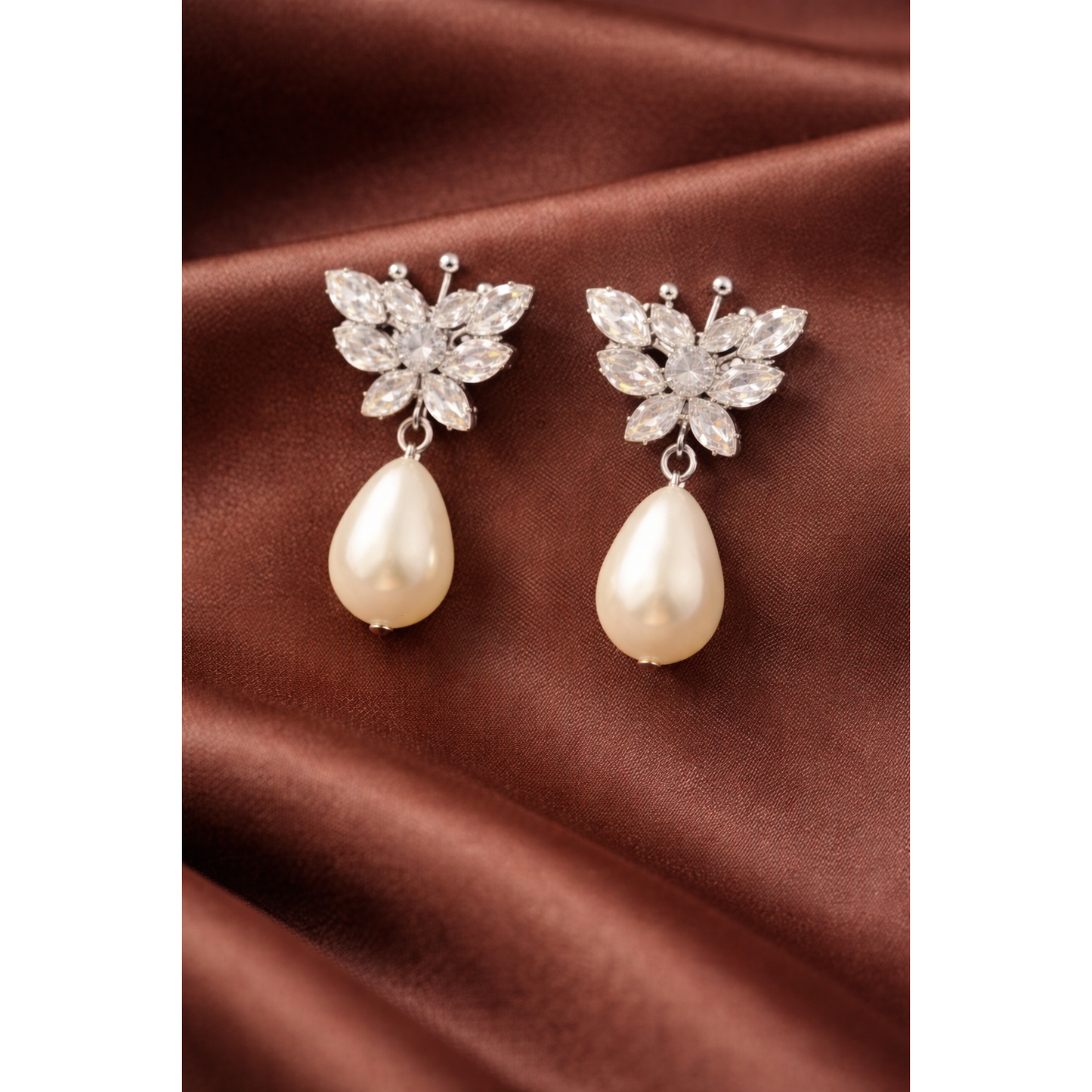 Silver butterfly crystal pearl drop earrings on brown satin fabric with soft folds and professional jewelry photography styling