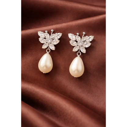 Silver butterfly crystal pearl drop earrings on brown satin fabric with soft folds and professional jewelry photography styling