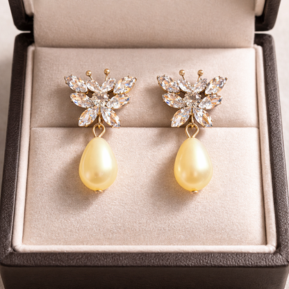 Gold butterfly crystal pearl drop earrings displayed inside a fine jewelry box with soft neutral velvet and high-definition lighting