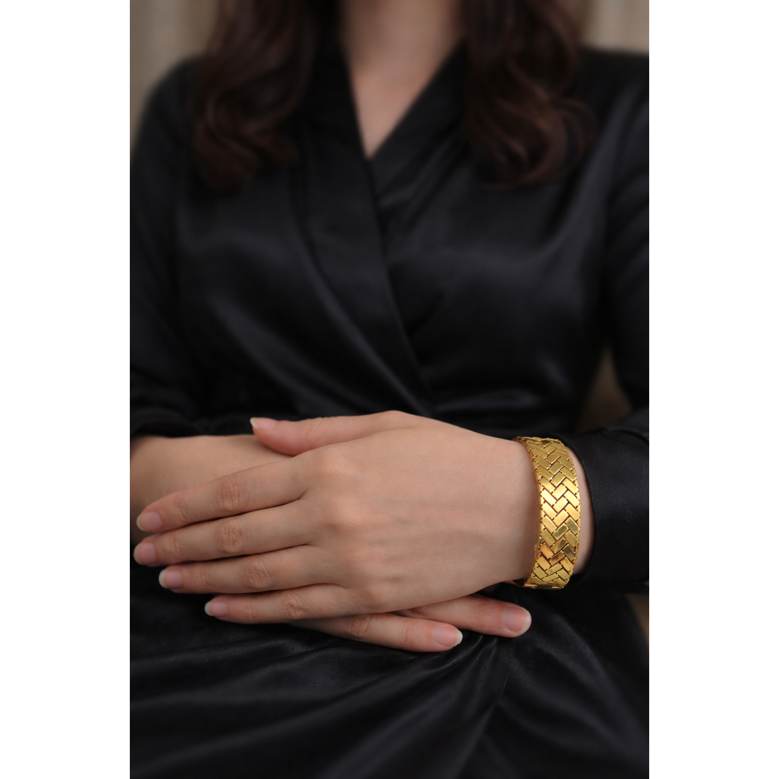 Gold herringbone lock bracelet worn on model wrist with black satin outfit, high polish woven cuff design