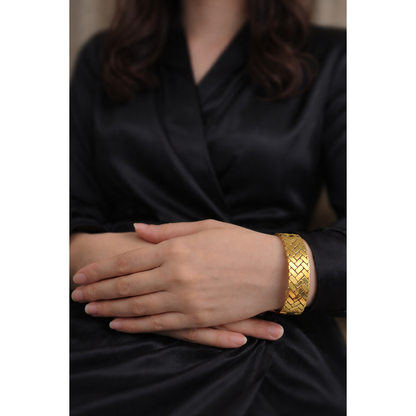 Gold herringbone lock bracelet worn on model wrist with black satin outfit, high polish woven cuff design
