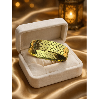 Gold herringbone lock bracelet displayed in cream velvet jewelry box on gold satin cloth with soft lantern background