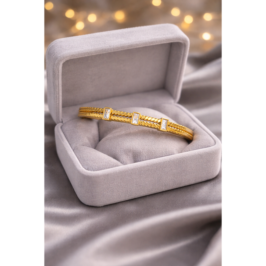 Gold lock bracelet with crystal accents displayed in light grey velvet jewelry box on grey satin cloth with blurred fairy lights backgroun