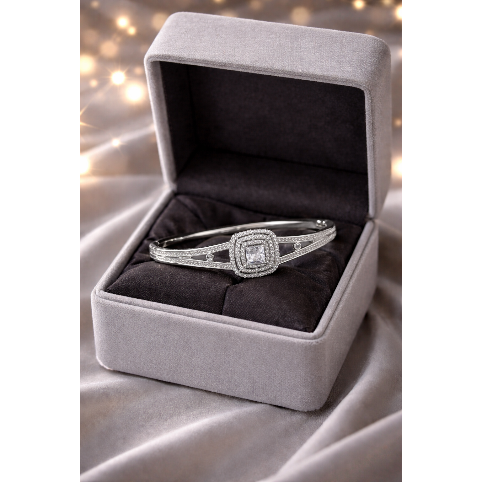Silver Art Deco square halo bracelet with secure lock closure displayed in light grey velvet jewelry box on satin grey cloth with blurred fairy lights