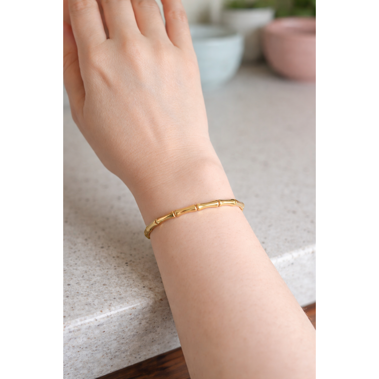 Gold bamboo link bracelet with lock worn on feminine hand on a counter with soft background