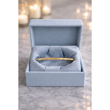 Gold bamboo link bracelet with lock displayed in smokey blue velvet box on grey marble with blurred candles